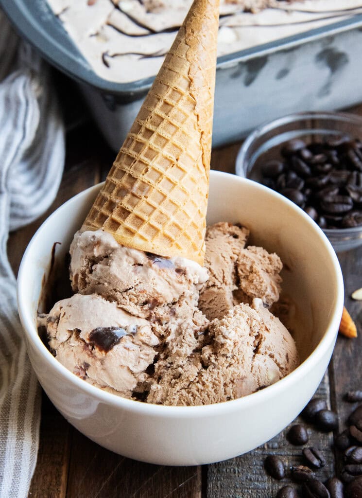 A bowl of mocha ice cream with a swirl of fudge and almond pieces.