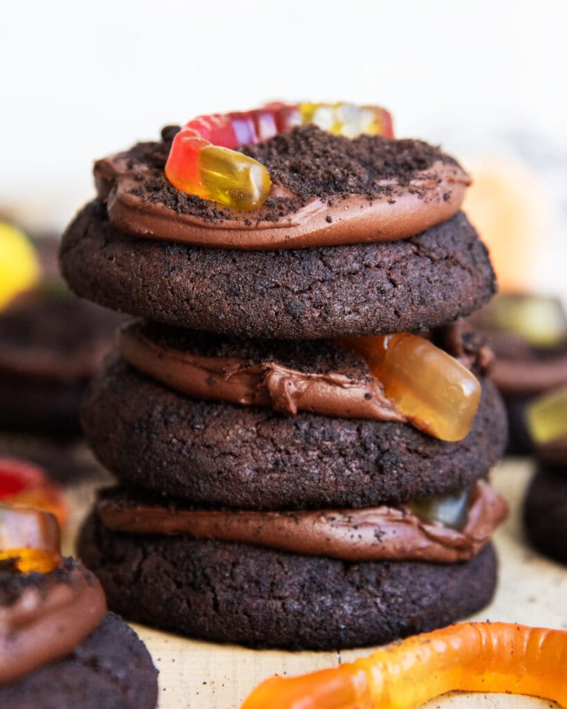 A stack of three large dirt cake chocolate cookies with oreo crumbs and a gummy worm on top. 