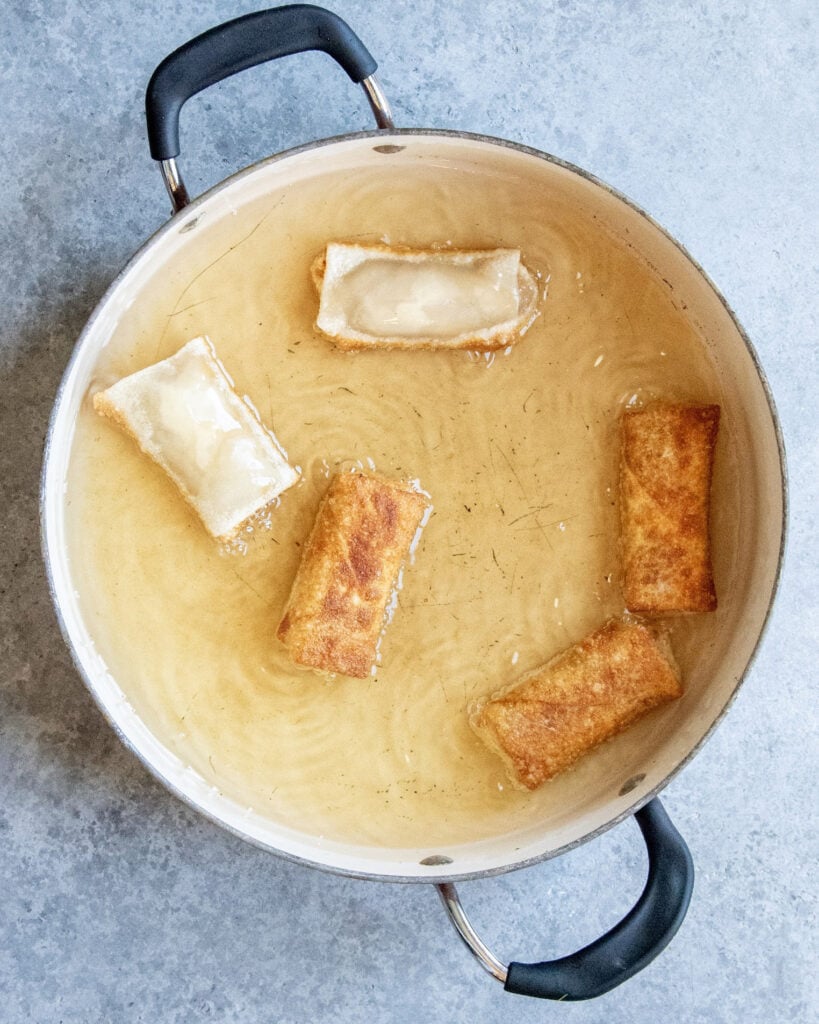Egg rolls being fried in a pot of oil.