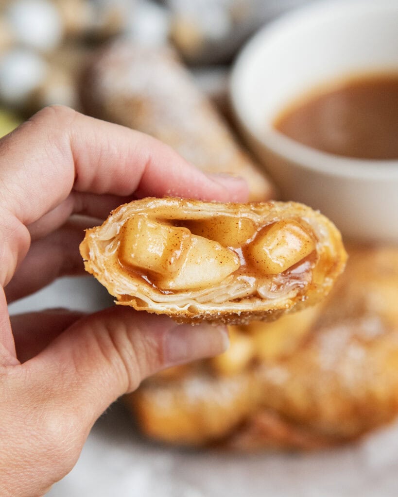 A hand holding a half of an apple pie egg roll with juicy apple pie filling in the middle.