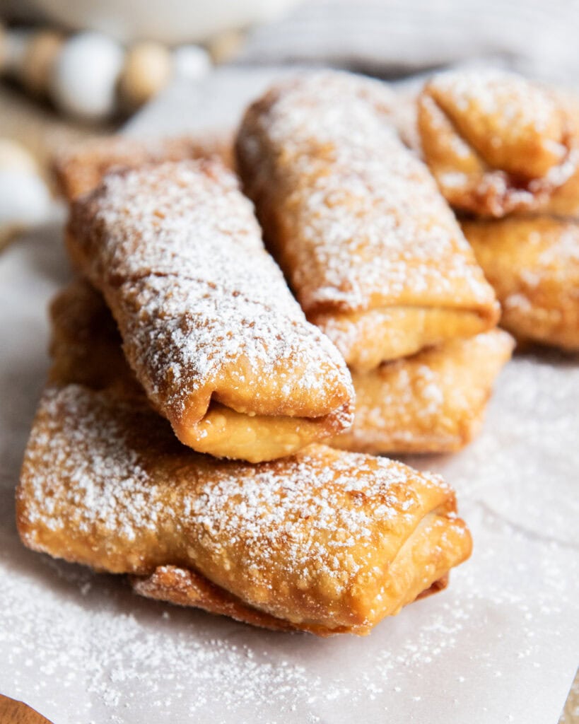 A stack of apple pie egg rolls dusted with powdered sugar.