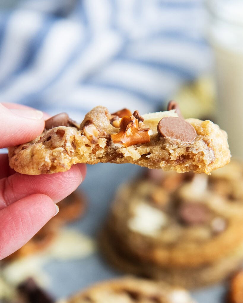 A hand holding a chocolate chip cookie with a bite out of it.