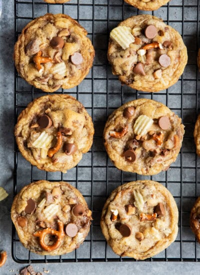 An above view of sweet and salty cookies on a cooling rack with pretzels, potato chips, and chocolate chips.