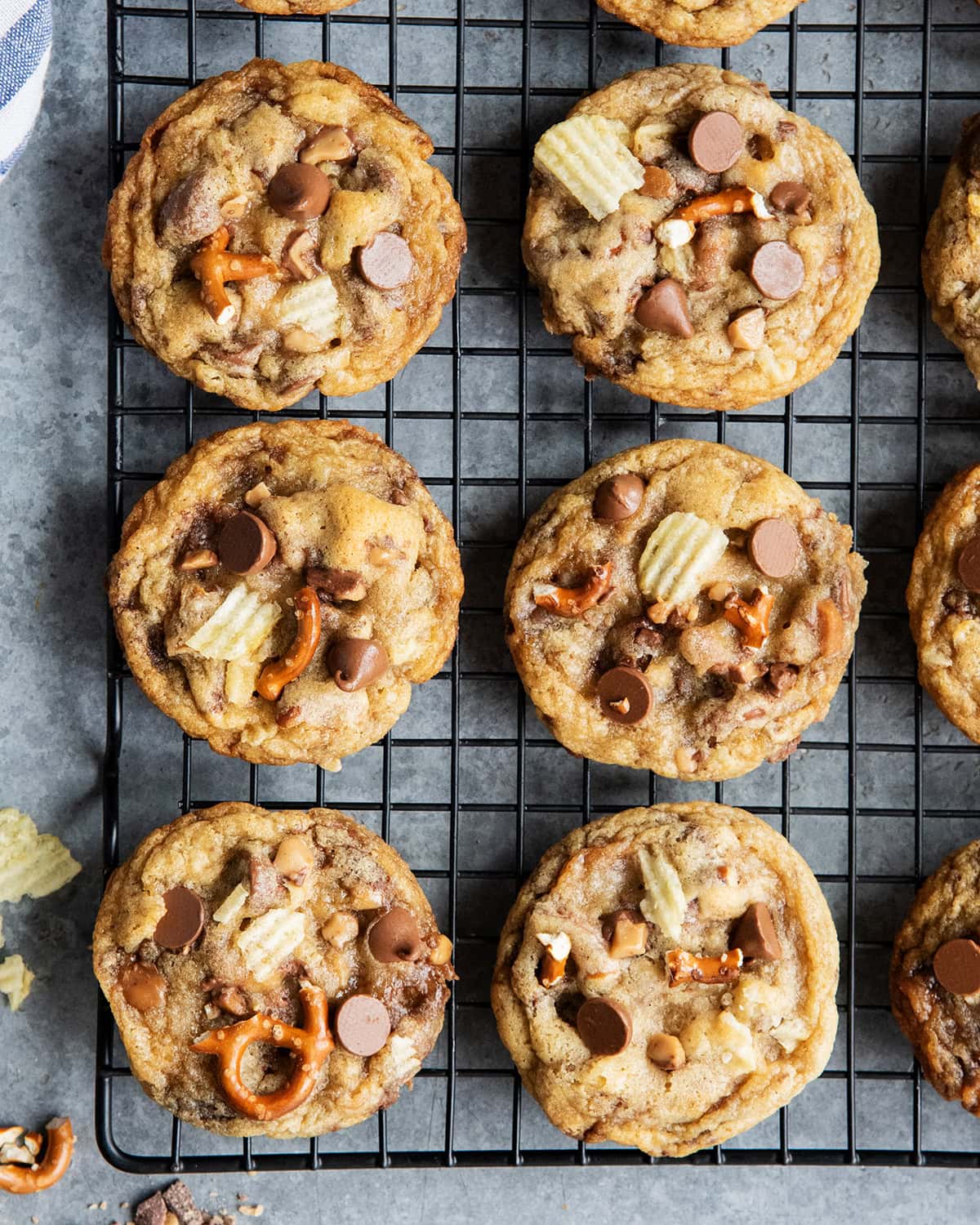 An above view of sweet and salty cookies on a cooling rack with pretzels, potato chips, and chocolate chips.