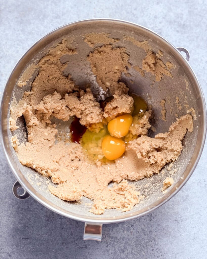 A bowl of creamed butter and sugar topped with two raw eggs.