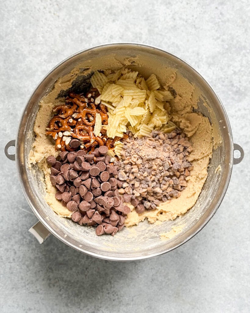 A bowl of cookie dough topped with chips, pretzels, chocolate chips, and toffee bits.