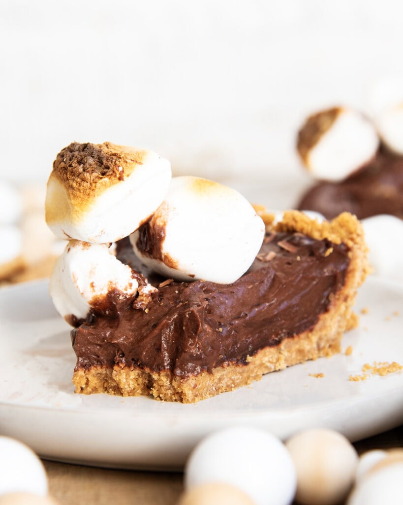 A piece of s'mores pie on a plate with a bite removed on the front.