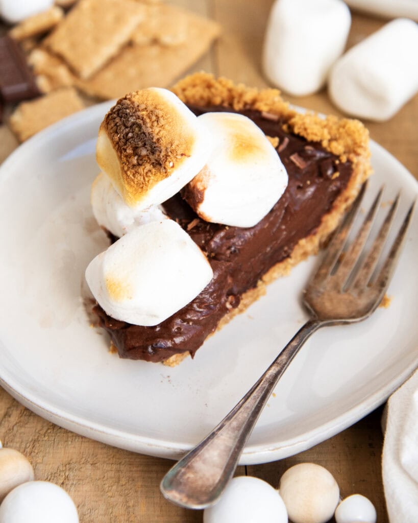 A piece of chocolate s'mores pie on a plate next to a fork.