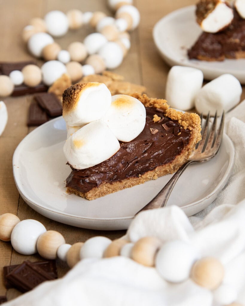 A piece of chocolate s'mores pie on a plate next to a fork.