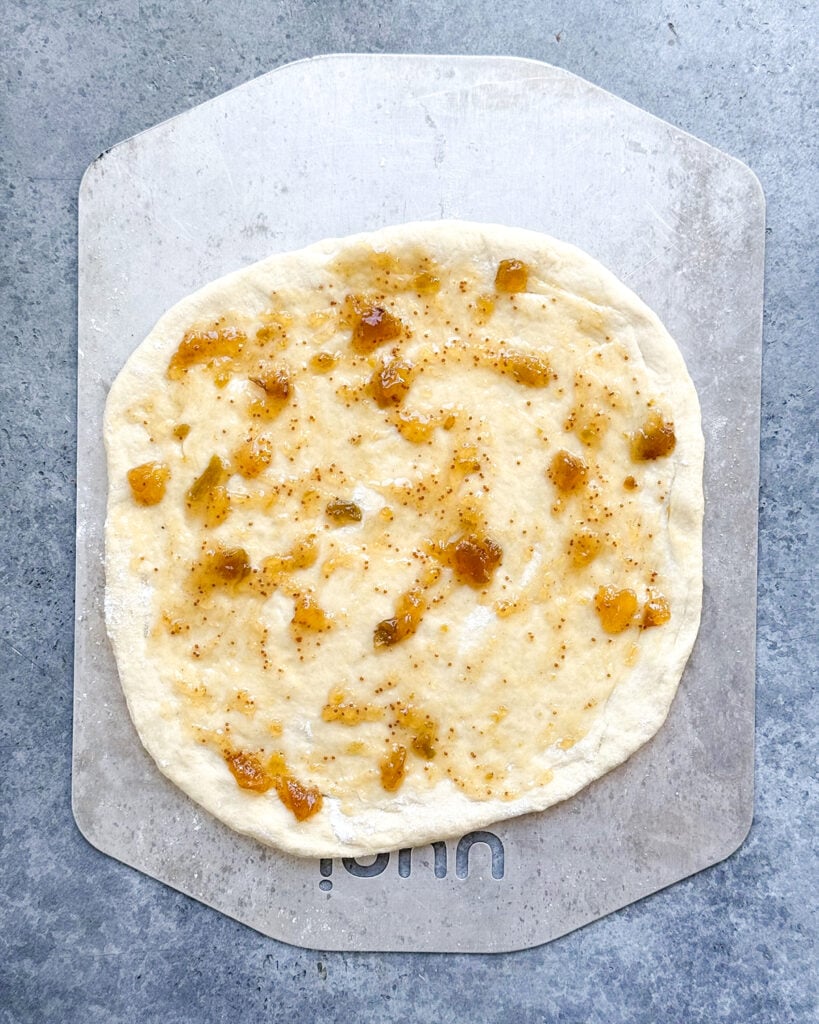 Raw pizza dough topped with fig jam on a metal pan.