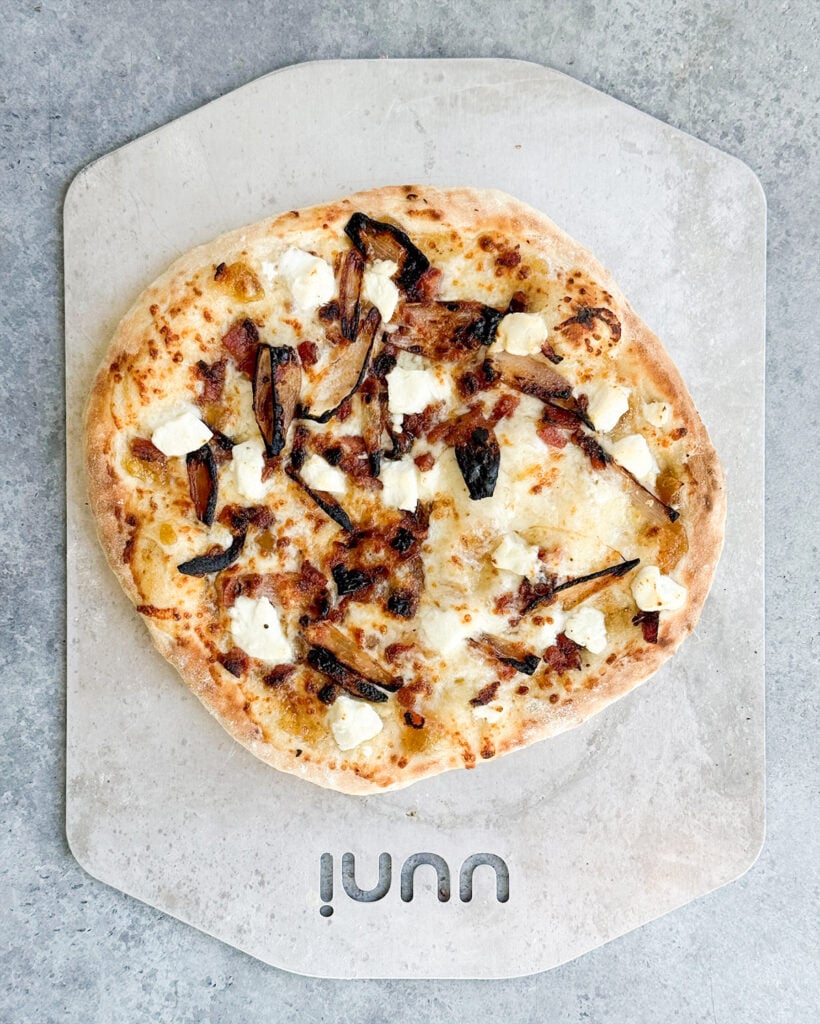 An above view of a goat cheese pizza topped with shallots and bacon.