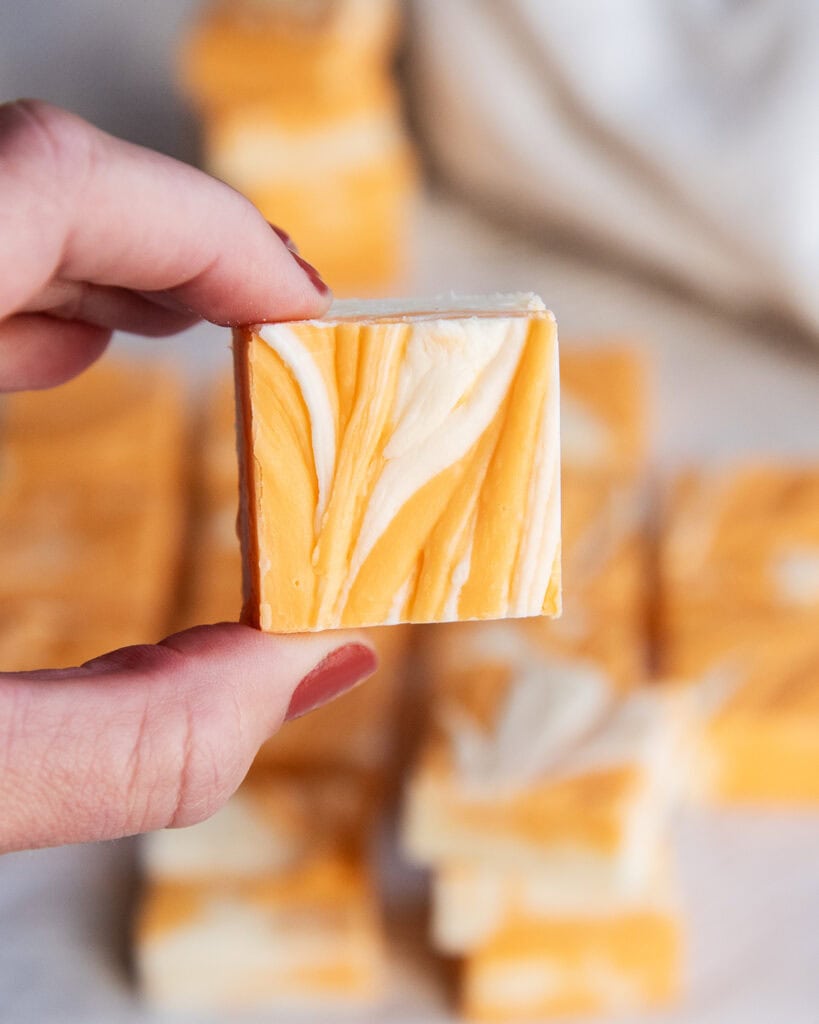 A hand holding a piece of creamsicle fudge swirled with orange and white colors..