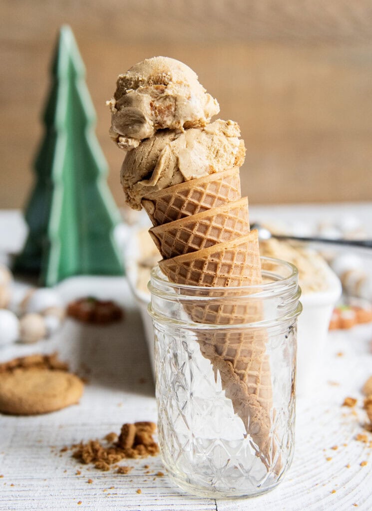 An ice cream cone topped with two scoops of gingerbread cookie ice cream sitting in a glass jar.
