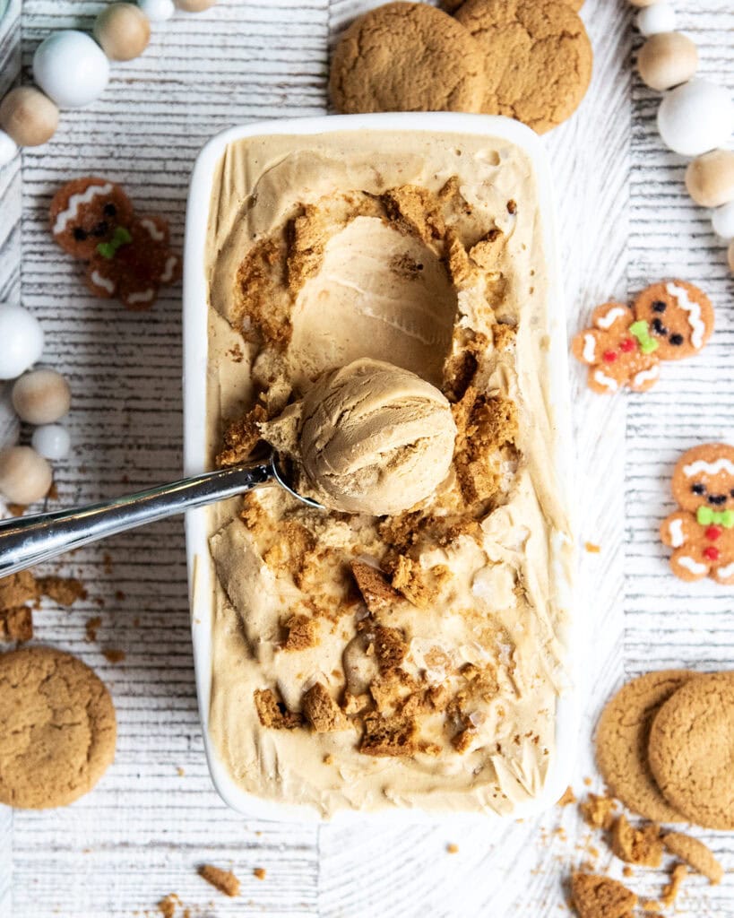 An above view of a container full of gingerbread ice cream with a scoop sitting on top.