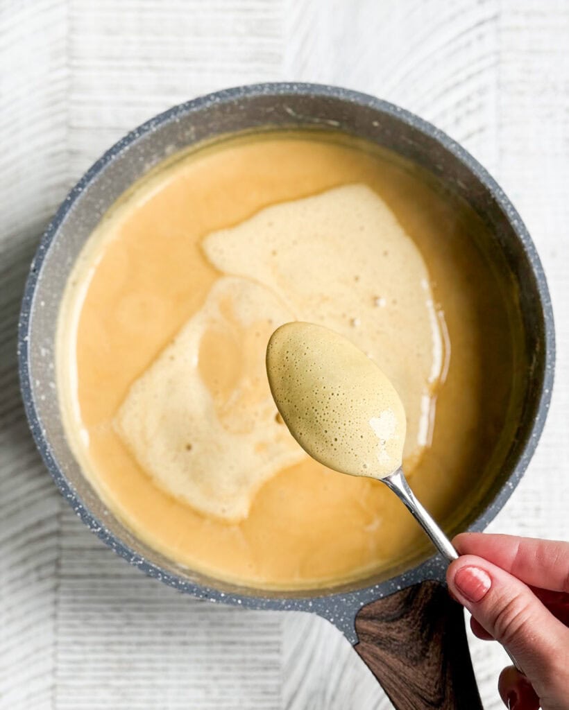 Gingerbread custard ice cream in a pot, with a spoon showing the thickened mixture above it. 
