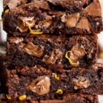 A stack of brownies with fudgy melted chocolate pieces and orange zest on them.