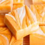 A pile of orange cream fudge marbled with white and orange fudge.