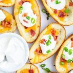 A tray of baked potato skins topped with cheese, sour cream, and bacon.