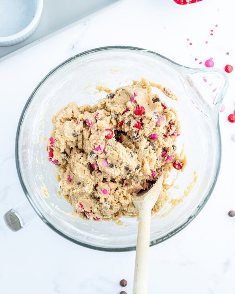 Cookie dough in a bowl loaded with valentine m&ms, and chocolate chips.