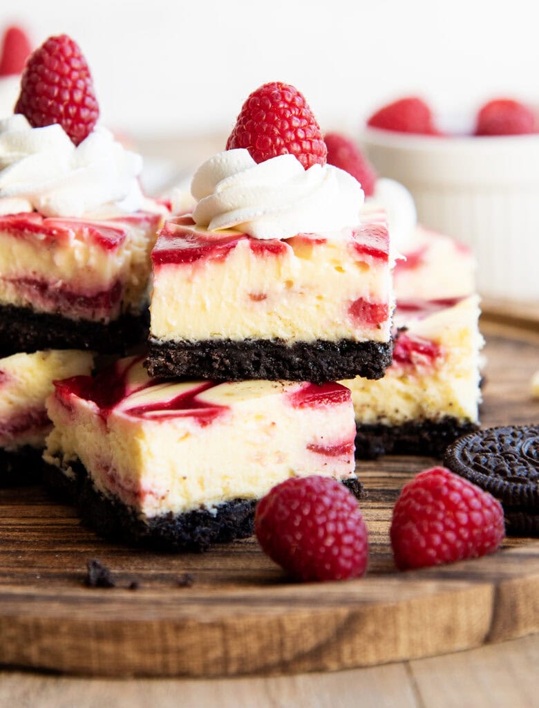 A pile of white chocolate raspberry cheesecake bars on a wooden board.