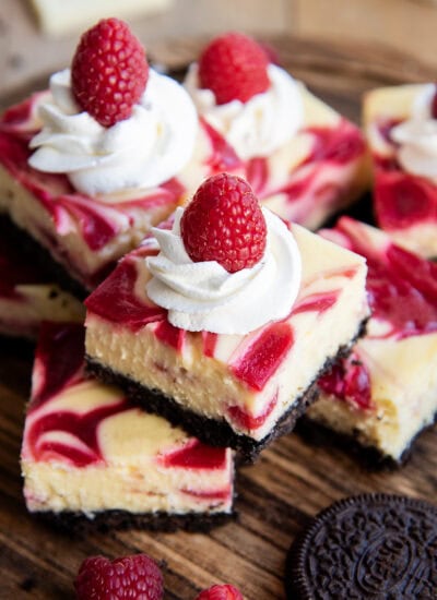 A pile of white chocolate raspberry cheesecake bars on a wooden board.