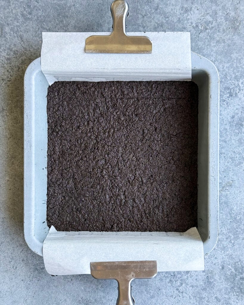 A baked oreo crust in a square pan.