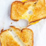 Two garlic butter grilled cheese sandwiches being split in half showing the gooey cheese in the middle.