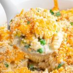 A scoop of tuna casserole on a spoon, above a pan of the casserole.