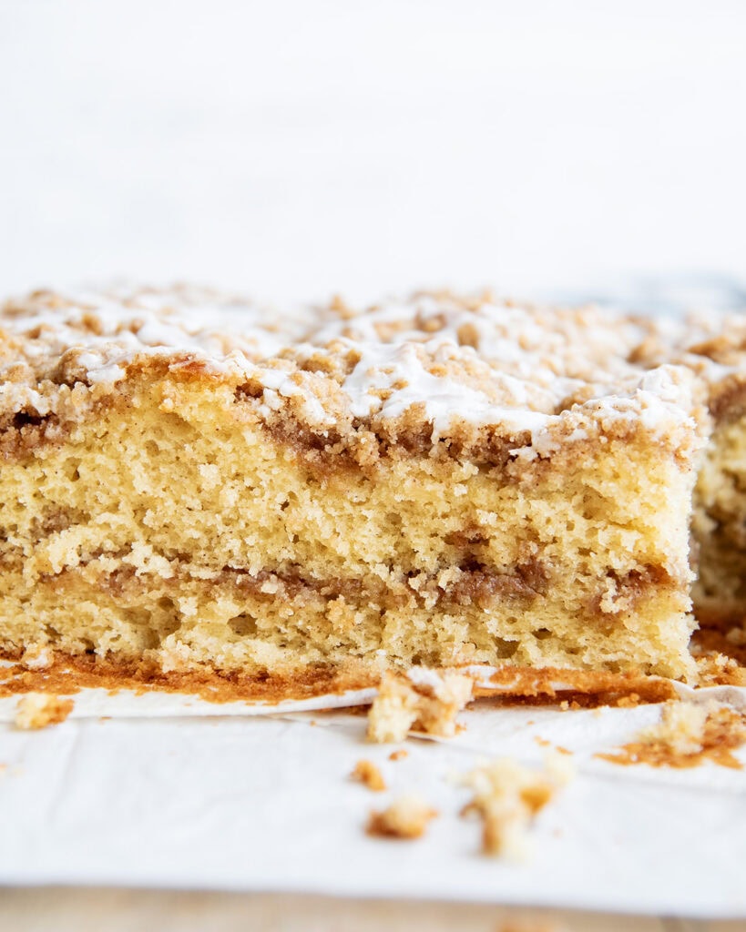 A side view of cinnamon swirl coffee cake with a swirl of cinnamon and topped with a crumb topping and icing.