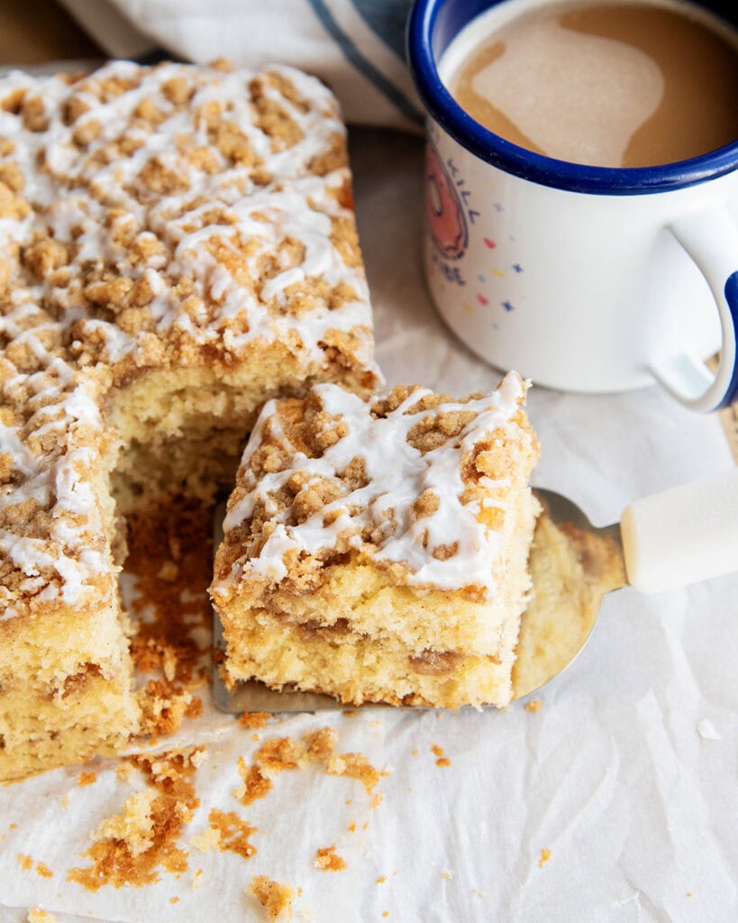 A piece of cinnamon coffee cake on a metal spatula next to a mug of coffee.