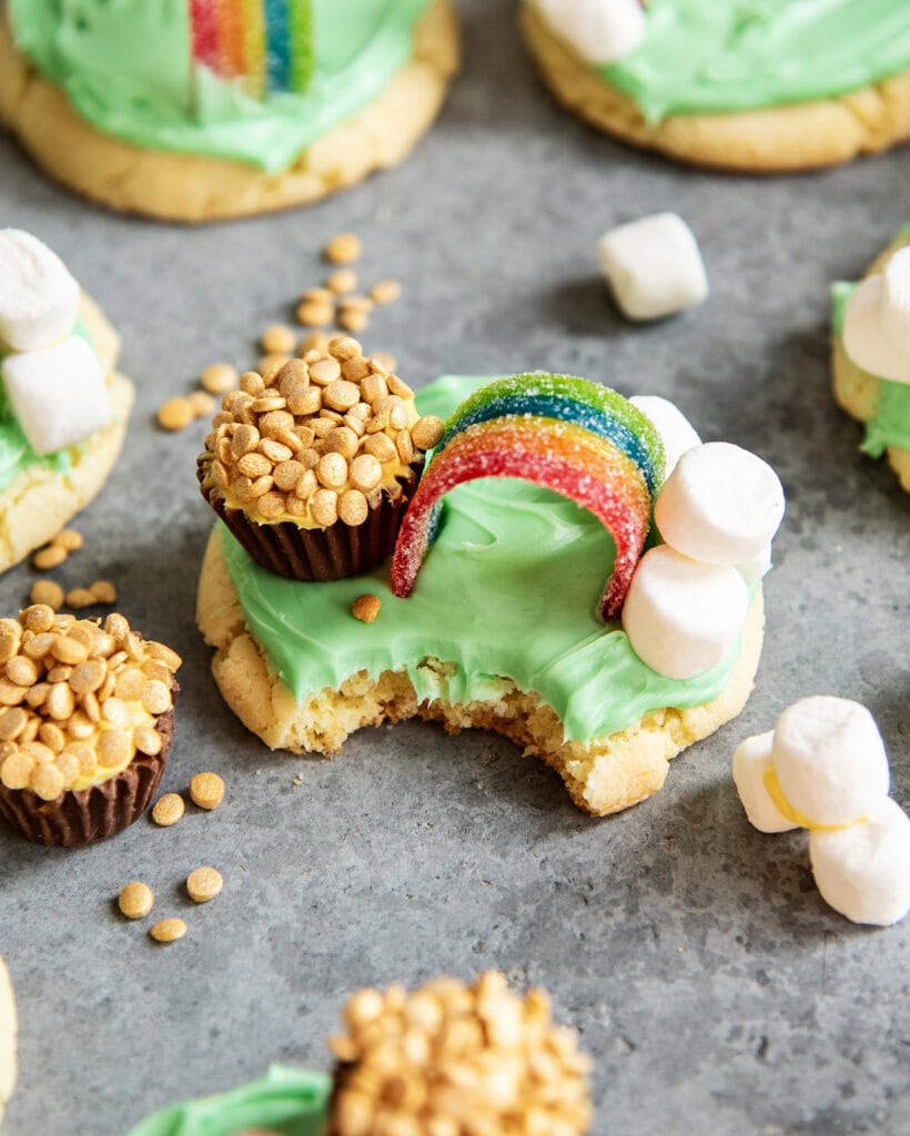 A "pot of gold" cookie decorated with a candy rainbow, cloud marshmallows, and a reeses cup pot of gold, with a bite out of it.