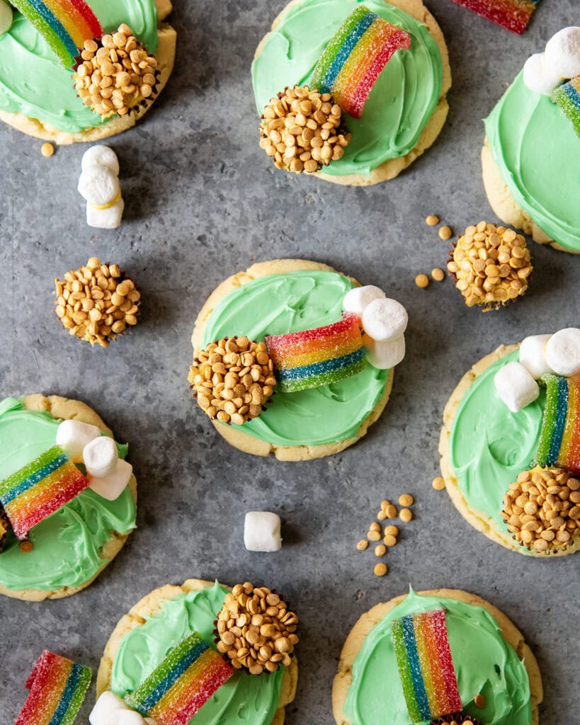 An above view of green frosted cookies topped with marshmallows, a rainbow candy and a peanut butter cup decorated to look like a pot of gold.