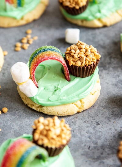 A green frosted sugar cookie topped with marshmallows, a rainbow candy and a peanut butter cup decorated to look like a pot of gold.