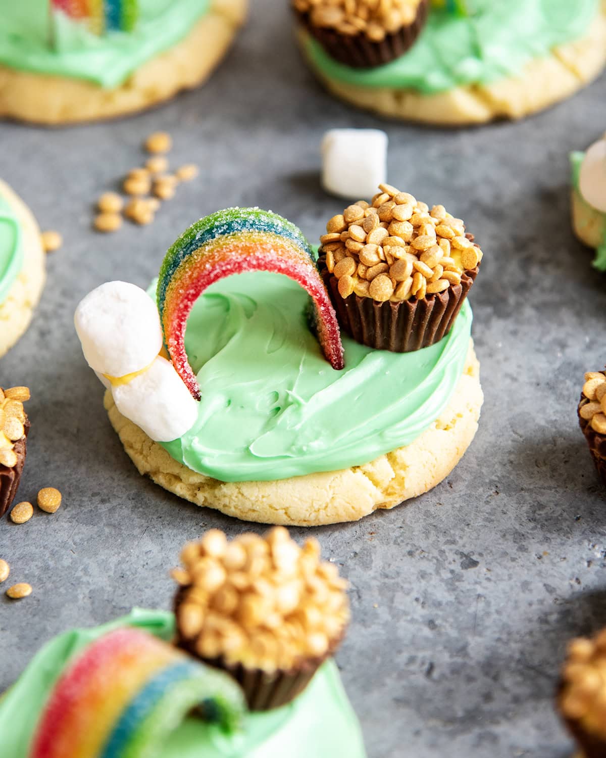 A green frosted sugar cookie topped with marshmallows, a rainbow candy and a peanut butter cup decorated to look like a pot of gold.
