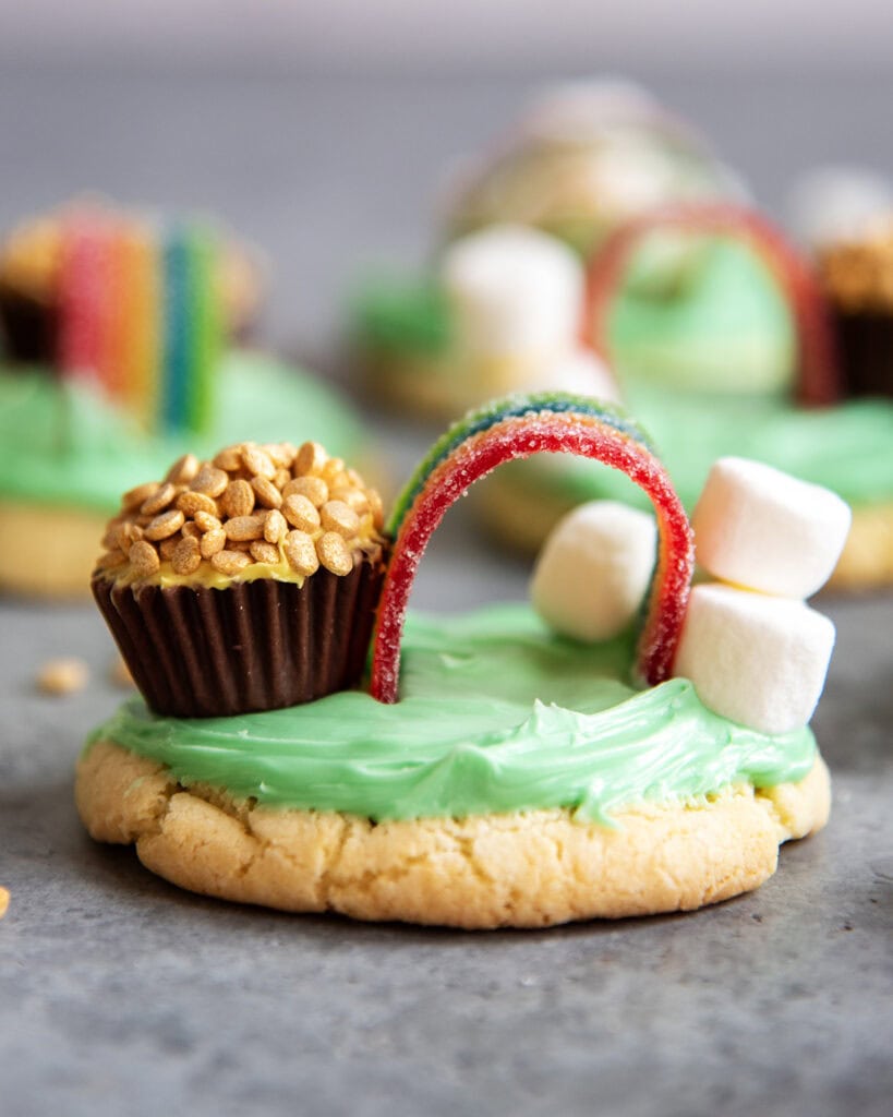 A green frosted sugar cookie topped with marshmallows, a rainbow candy and a peanut butter cup decorated to look like a pot of gold. 
