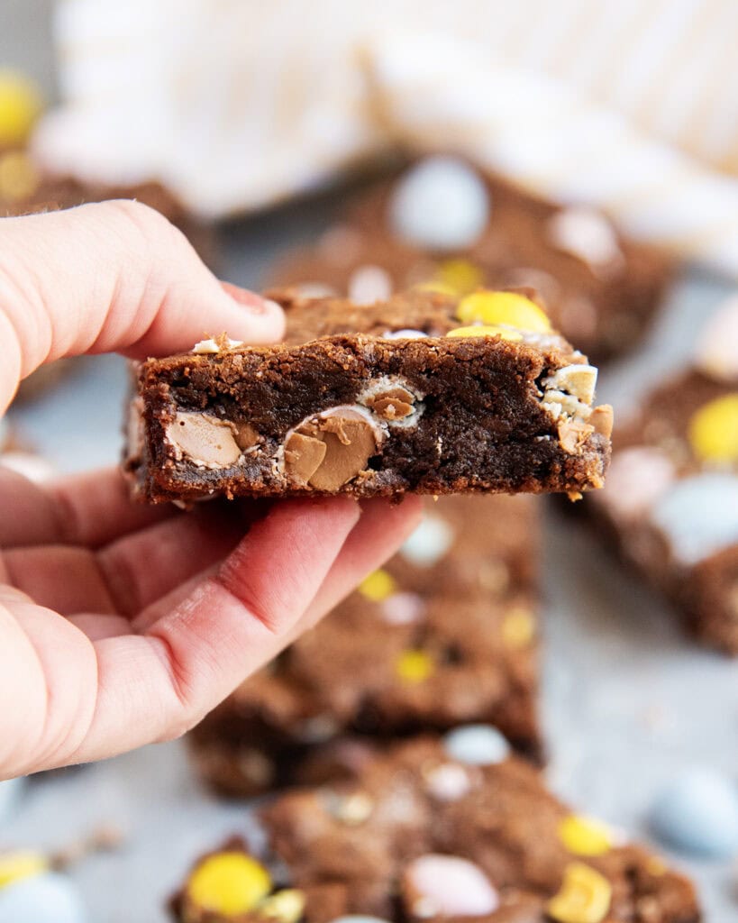 A hand holding a cadbury mini egg filled brownie piece.
