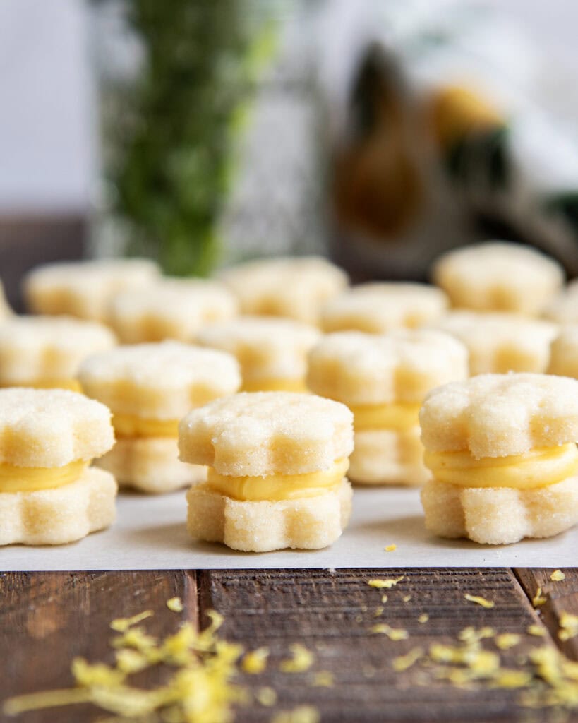 A side view of tiny lemon sandwich cookies on a piece of parchment paper.