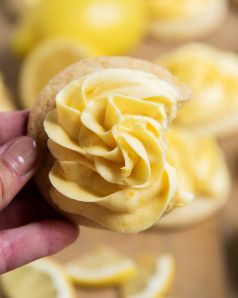 A hand holding a lemon frosted sugar cookie with a bite out of it.