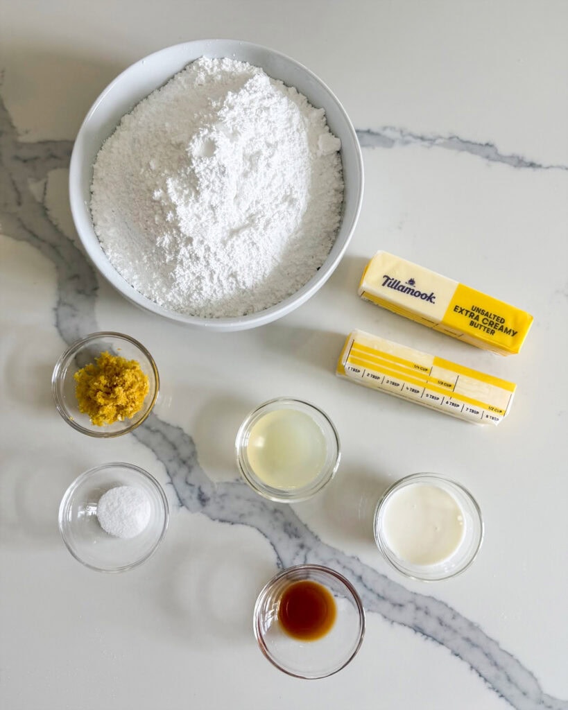 Small bowls of the ingredients needed to make lemon buttercream frosting, including butter, powdered sugar, lemon zest, vanilla, and salt. 