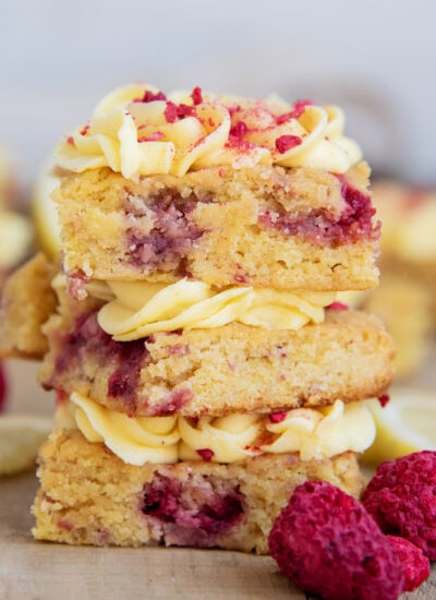 A stack of three raspberry lemon blondies with lemon frosting on top.