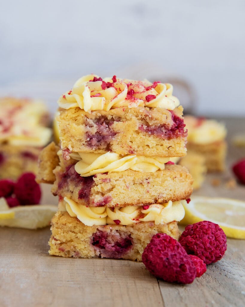 A stack of three raspberry lemon blondies with lemon frosting on top.
