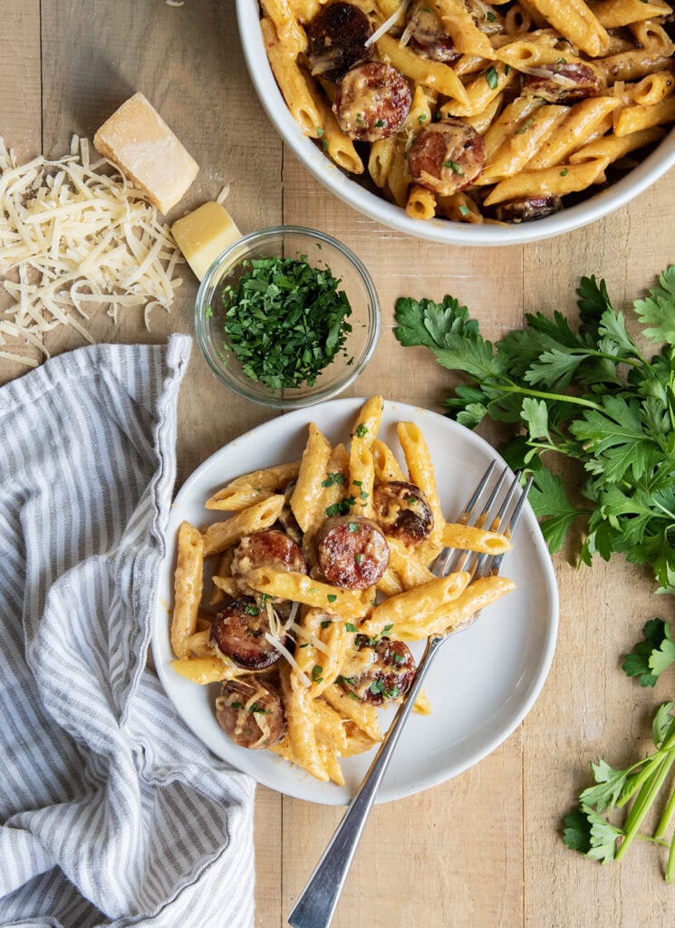 A plate of sausage alfredo pasta next to a big bowl of it.