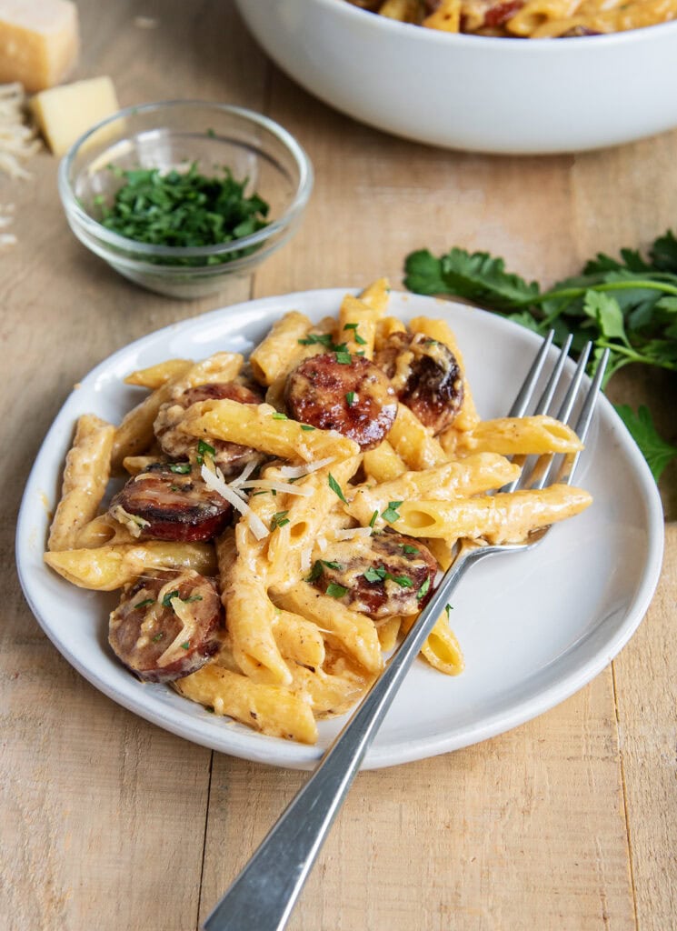 A plate of sausage alfredo pasta next to a big bowl of it.