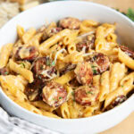 A bowl of penne pasta and sausage coated in a creamy cajun alfredo sauce.