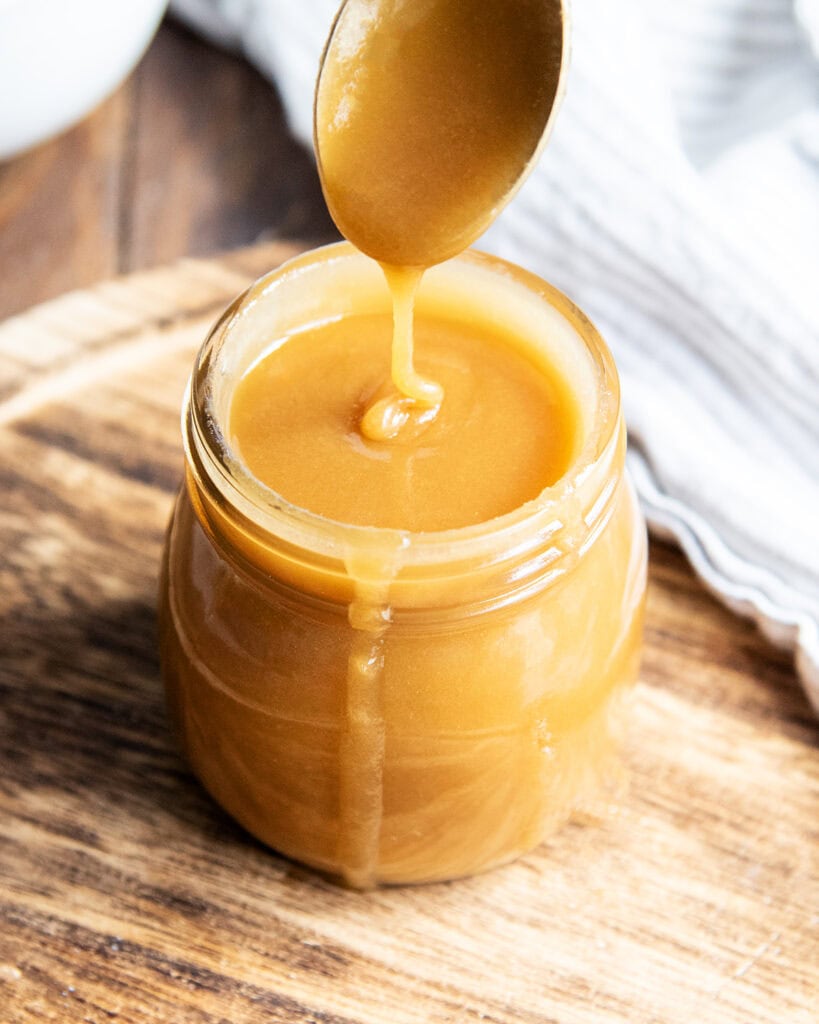 Butterscotch sauce drizzling from a spoon into a jar,
