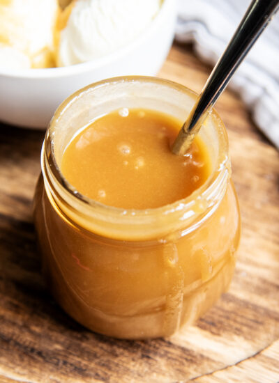 A jar of butterscotch sauce with a spoon in the jar and sauce dripping over the side.