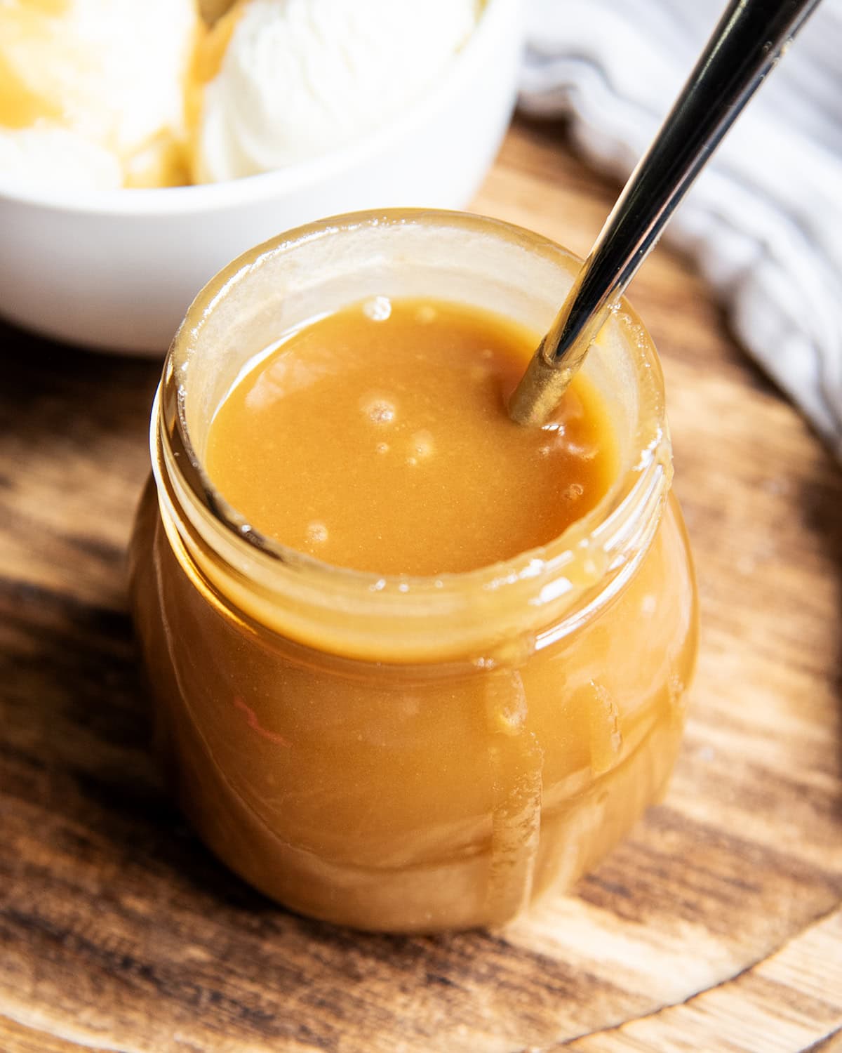 A jar of butterscotch sauce with a spoon in the jar and sauce dripping over the side.