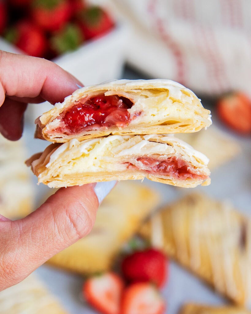 A hand holding two halves of a strawberry cheesecake hand pie.