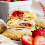 A stack of strawberry cheesecake hand pies and two are cut in half showing the filling.