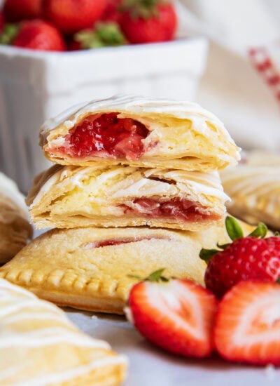 A stack of strawberry cheesecake hand pies and two are cut in half showing the filling.